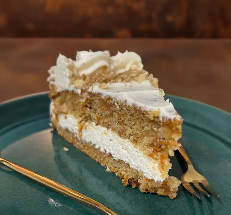 Porción de carrot cake con frosting y nueces, con una cuchara dorada