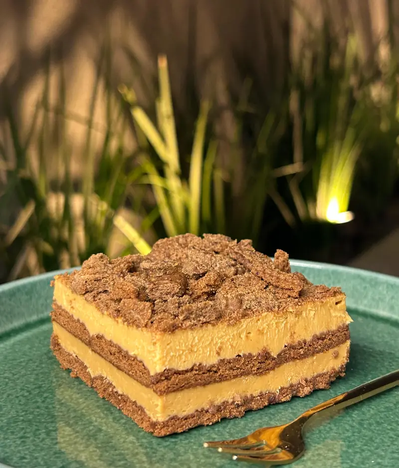Porción de chocotorta con capas de galletitas y crema, en plato verde con tenedor dorado