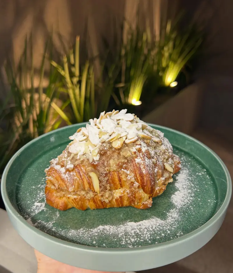 Croissant almendrado cubierto de almendras laminadas y azúcar impalpable, en plato verde