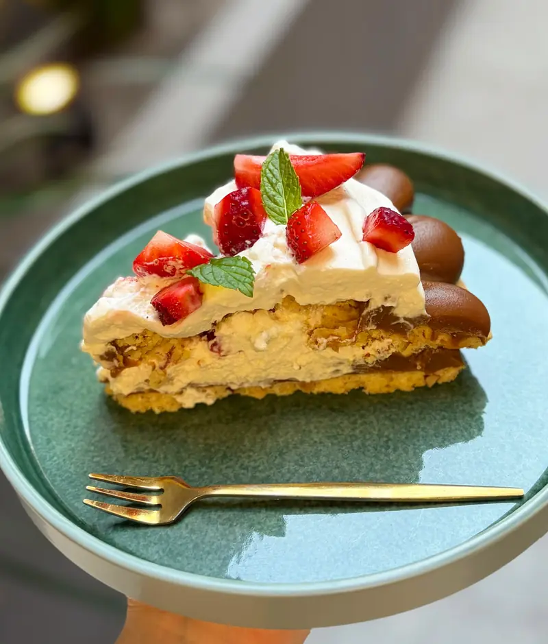 Porción de tarta de masa de almendras con dulce de leche, crema y frutillas
