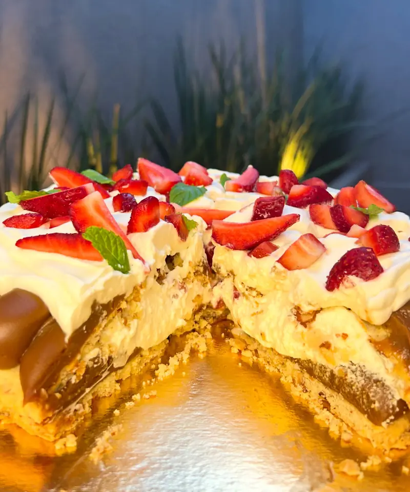 Tarta de masa de almendras con dulce de leche, crema y frutillas, recién cortada